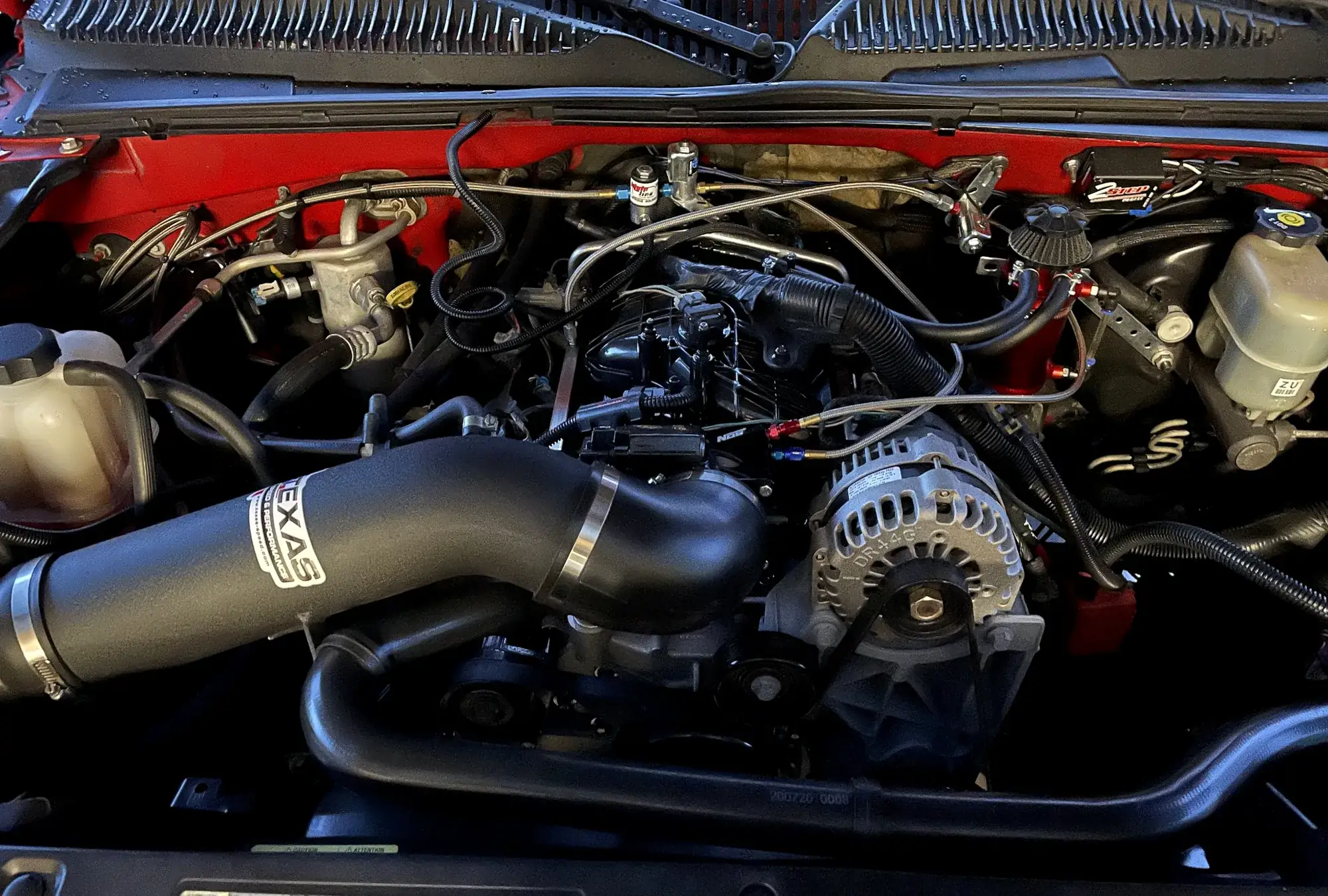 The engine bay of a red Chevy truck at our shop: the alternator, belts and a black Texas Speed intake tube