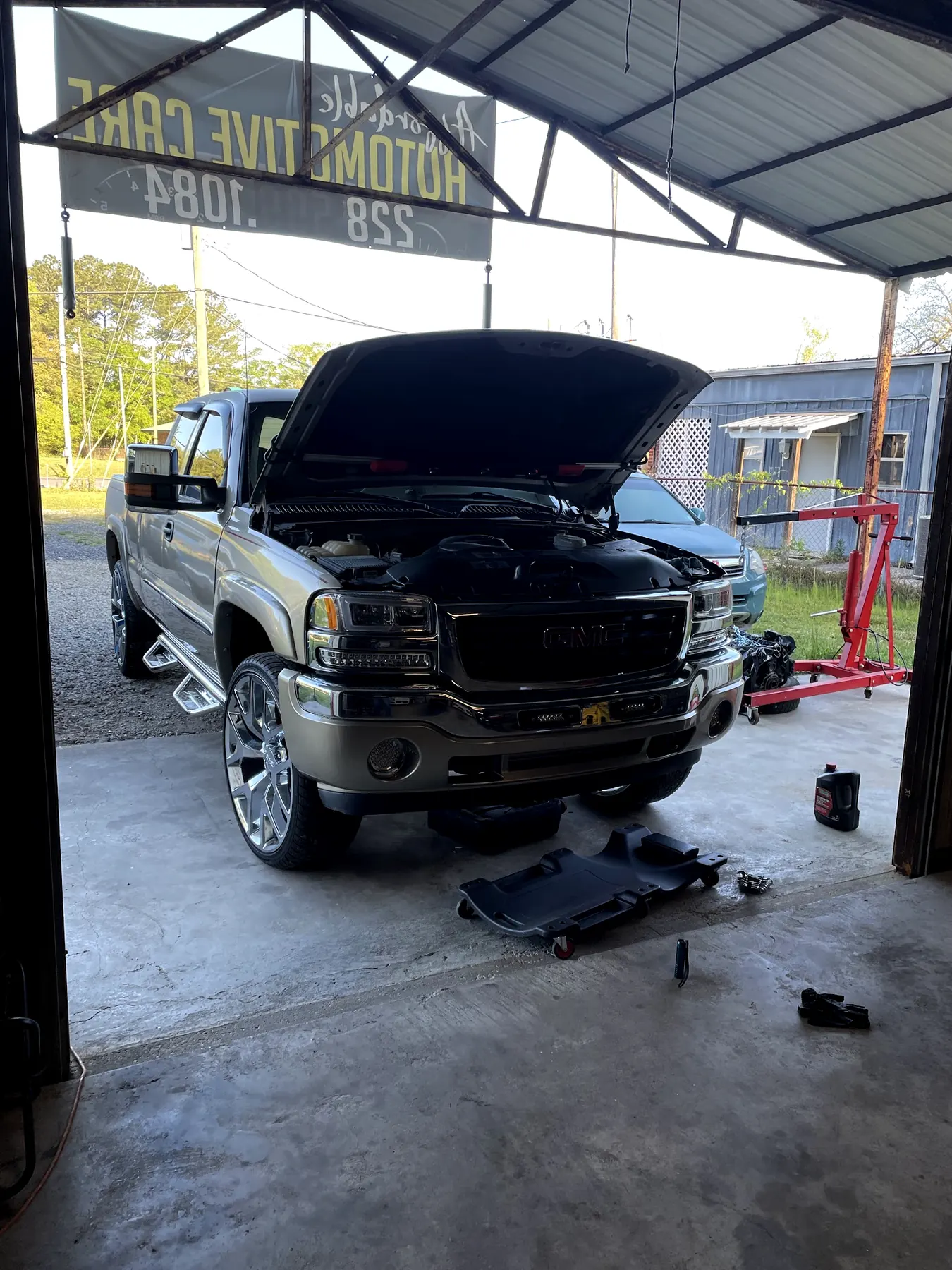 A GMC pickup with its hood up in our open bay, a creeper on the floor in front of it
