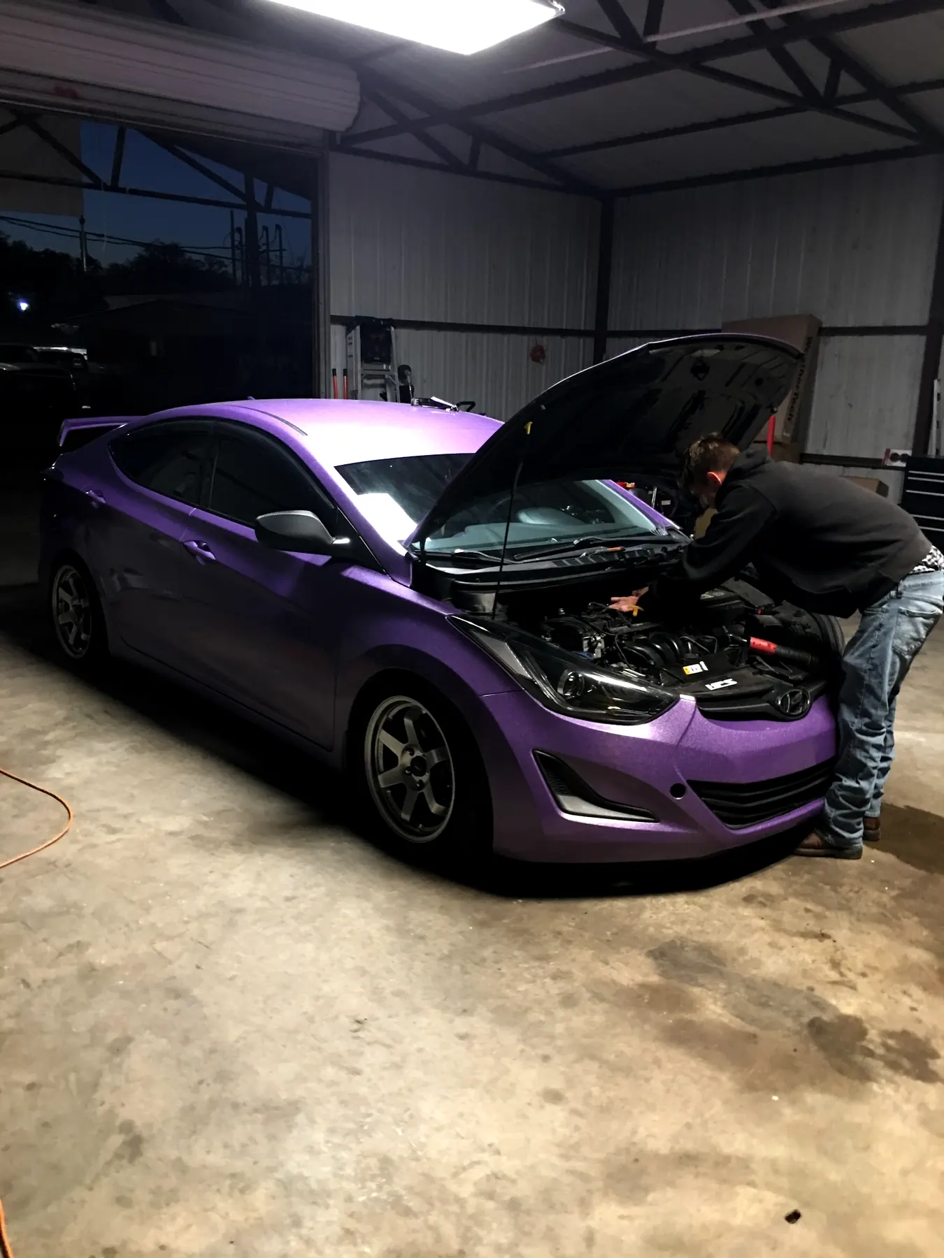 One of our mechanics leaning in under the open hood of a purple car inside our shop