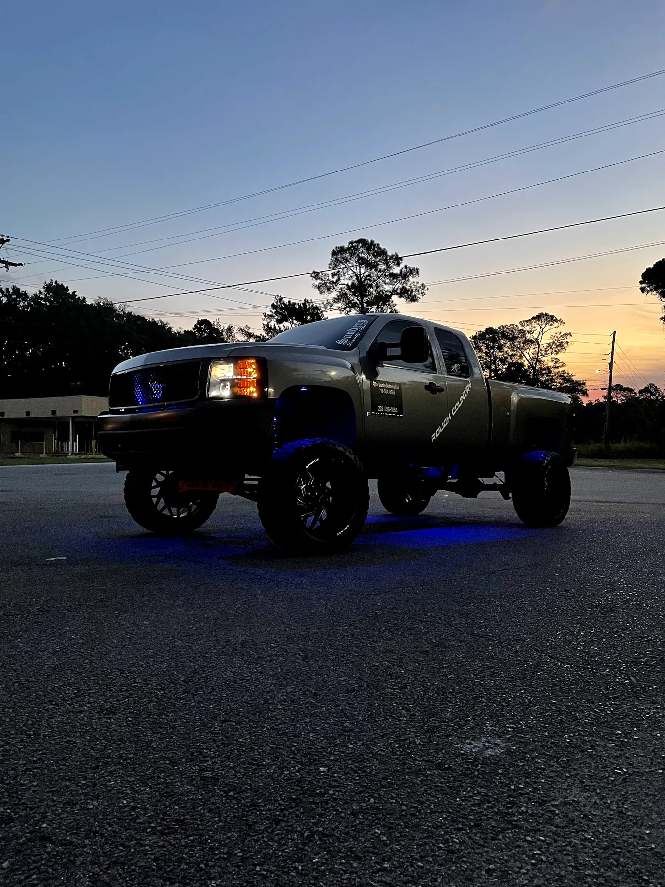 Our shop truck at dusk with its blue underglow on and the sunset behind the trees