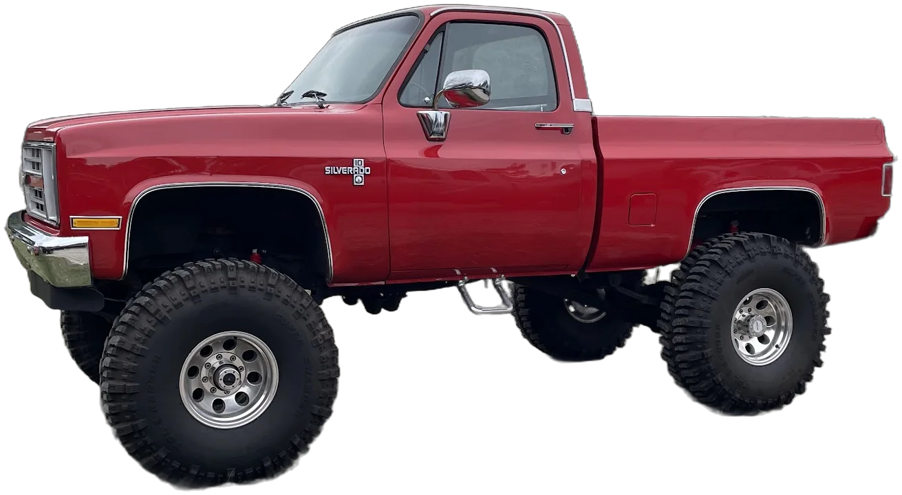A red lifted square-body Chevy Silverado on big mud tires, photographed on our lot