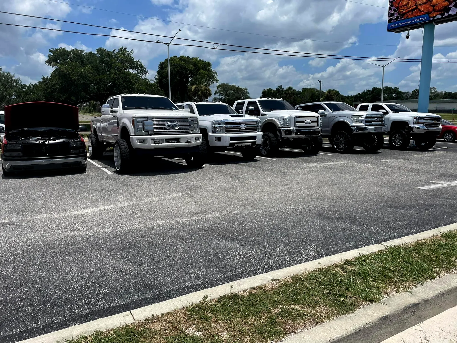 A row of big lifted pickups parked side by side under a wide sky